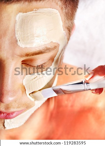 Man with clay facial mask in beauty spa.