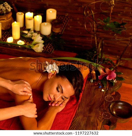 Aromatherapy massage of woman in spa salon. Girl on candles background treats problem health . Luxary interior with working masseuse. Indian back Massage as pain relief for female