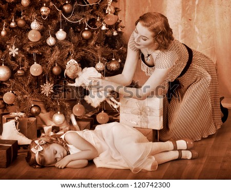 Child with mother receiving near Christmas tree. Black and white retro.