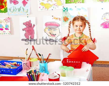 Child with scissors cut  paper  in playroom. Preschool.