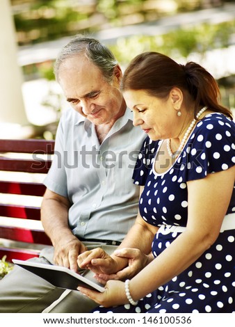 Old couple with tablet pc sit on bench  . Outdoor.