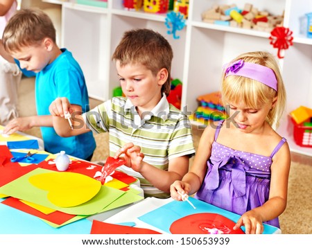 Child boy cutting out scissors paper in preschool.