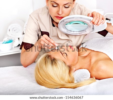 Woman getting tweezing eyebrow by beautician.