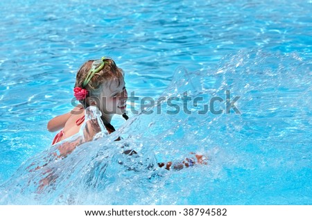 Girl with protective goggles and red bikini splashing in swimming pool.