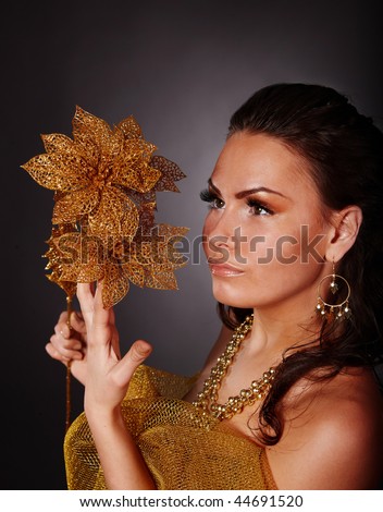 Beautiful young woman with gold flower on grey background.