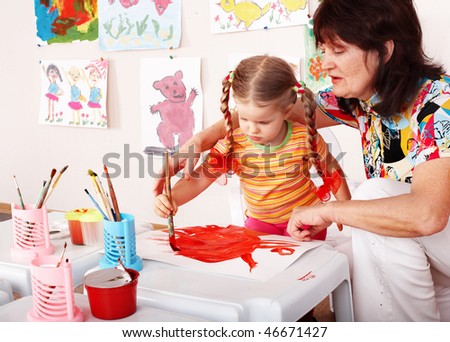 Child with teacher draw paints in playroom. Preschool.