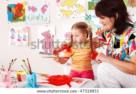 Child with teacher draw paints in playroom. Preschool.