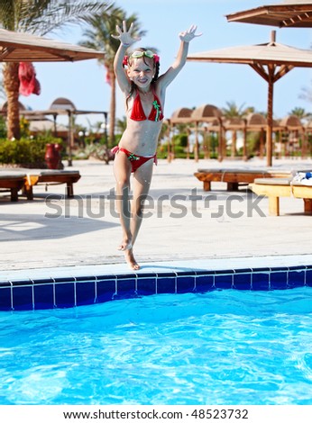 Girl with protective goggles and red swimsuit jump in swimming pool.