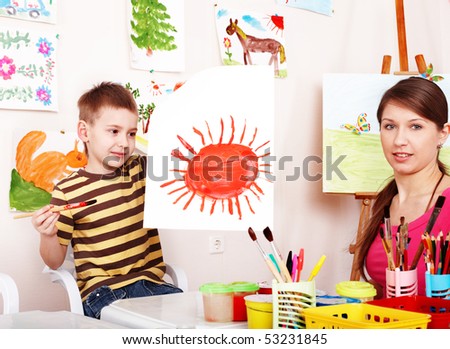 Child with teacher draw paint in play room. Preschool.