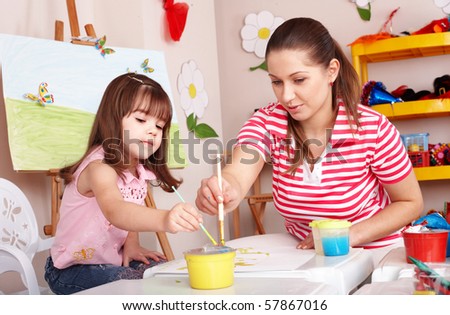 Child with teacher draw paints in play room. Preschool.