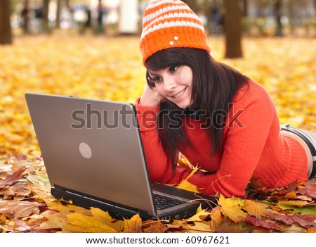 Young woman in autumn orange leaves with laptop. Fall sale. Outdoor.