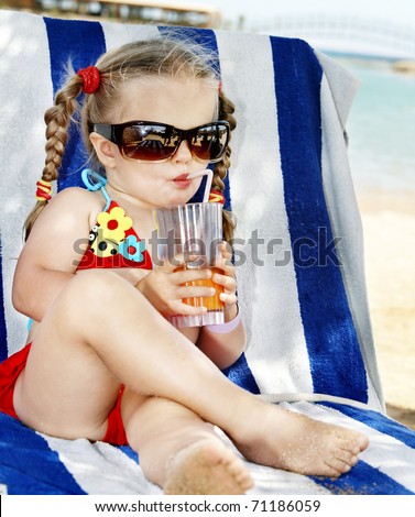 Little girl in glasses and red bikini drink orange juice.