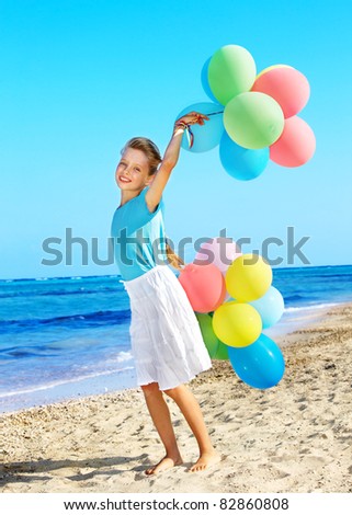 little girl playing with balloons at the beach.