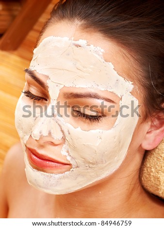 Beautiful girl having clay facial mask apply by beautician.