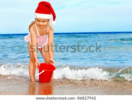 Child in santa hat playing on  beach. Summer New Year.