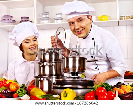 Happy man in chef hat and woman cooking at kitchen.