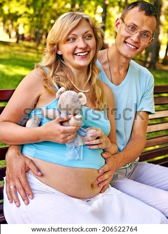 Pregnant woman with man  holding teddy bear outdoor in park.