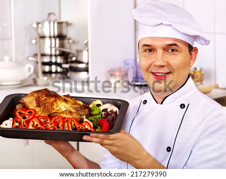 Happy man in chef hat cooking chicken.