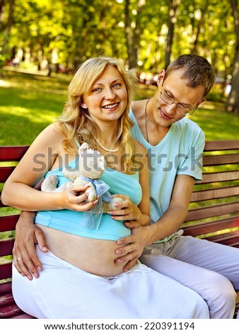 Pregnant woman with man  holding teddy bear outdoor in park.