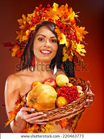 Girl with wreath of autumn leaves holding basket with fruit.
