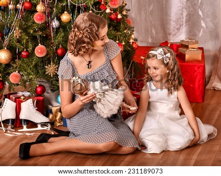 Child with mother receiving gifts under Christmas tree.