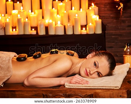 Young woman having Ayurveda stone massage. Many candles in background.