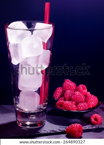 Red raspberry drink on black background. Empty glass with ice cube .