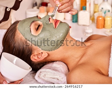Woman with clay facial mask in beauty spa. Close up.