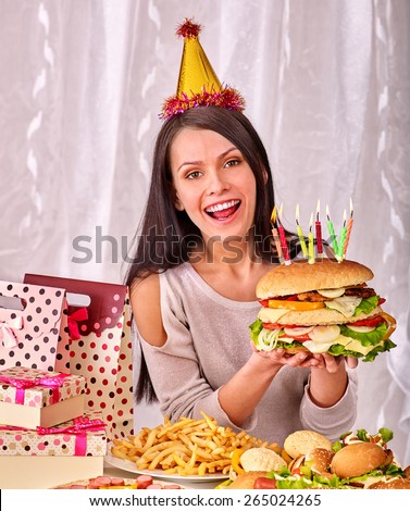 Woman wearing party hat eating hamburger at birthday. Shopping bag,