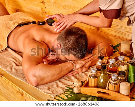 Man getting stone therapy massage in bamboo spa. Face is not visible.