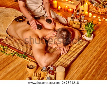 Man getting stone therapy massage in bamboo spa.
