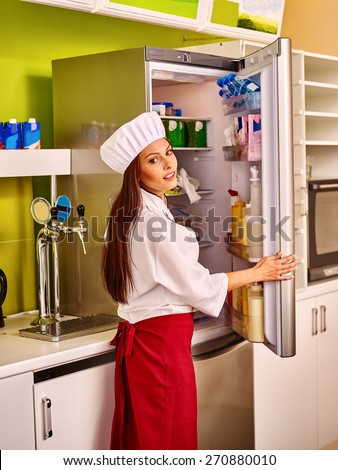 Female chef wearing uniform at cafeteria. Girl opens fridge.