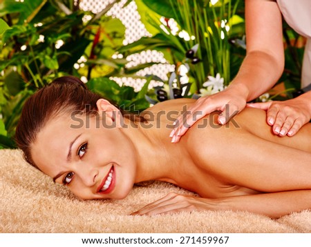 Woman getting massage in tropical spa. Plant background.