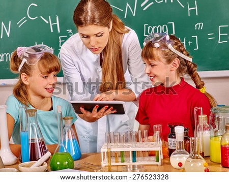 Children and teacher holding flask in chemistry class. Looking at pc.