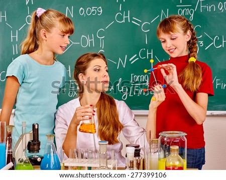 Teacher with children holding flask in chemistry class. Three people.