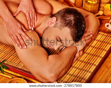 Handsome man getting massage in bamboo spa. Female therapist.