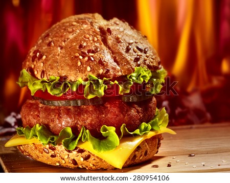 Double patty hamburger on wooden board on background of fire.