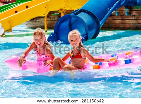 Kids are floating on inflatable mattress in water park. Summer holiday.