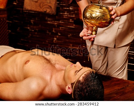 Young  handome man having Ayurveda spa treatment with pouring oil on head.
