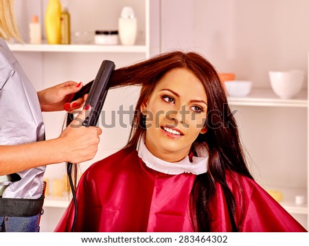 Woman at hairdresser with iron hair curler. Hair style.