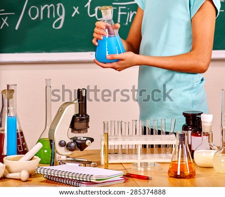 Kids hand holding flask in chemistry class with blackboard.