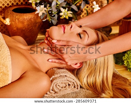 Woman with closrd eyes getting facial massage in tropical spa.