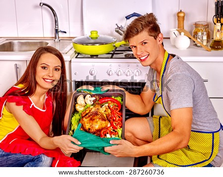 Happy couple cooking chicken at kitchen. Woman in red apron.