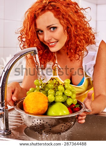 Happy woman washing fruit in colander at kitchen.
