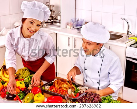 Happy man and woman in chef hat cooking chicken.