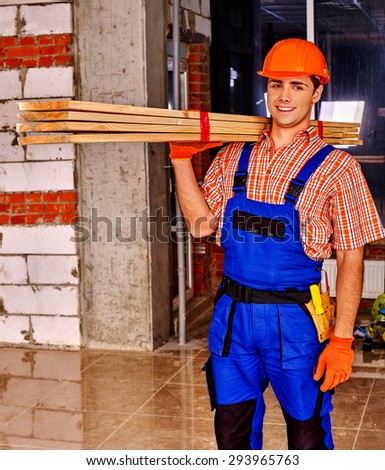 Happy man in builder uniform carry wooden boards indoor.