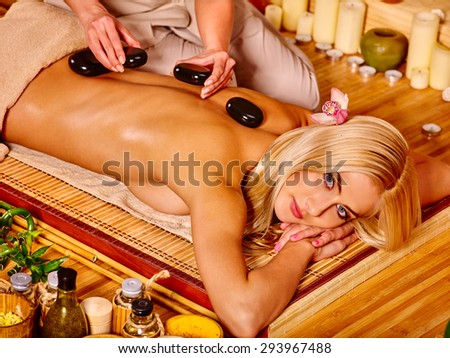 Woman getting stone therapy massage and looking at camera in bamboo spa.