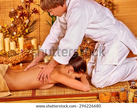Young woman getting bamboo massage. Male therapist kneels.