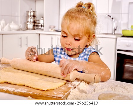 Child little girl with rolling-pin preparing dough at kitchen.