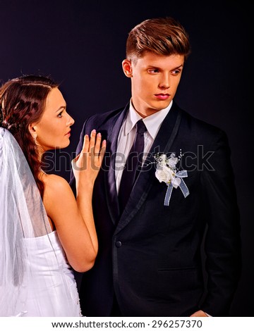 Bride and groom wearing wedding dress and costume on black background.